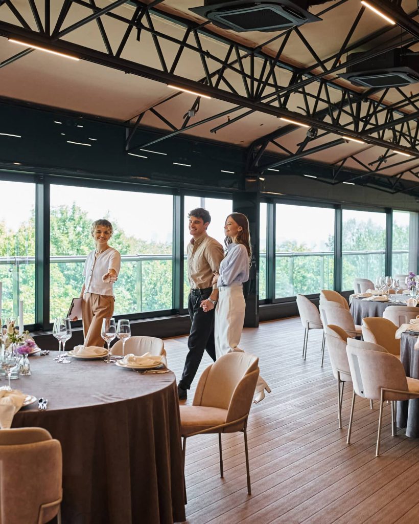 event organizer showing tables with festive setting to happy couple in decorated banquet hall